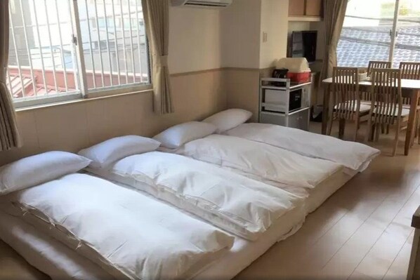 Una habitación con una cama grande, una kitchenette pequeña, una mesa de comedor con sillas y un ventanal con cortinas.