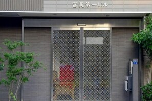 A building entrance with a metal gate, a sign above the gate, and a small tree to the left. - Uenohouse Family Room (Tokyo)