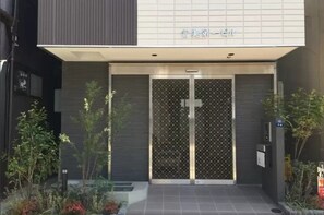 A modern building entrance with a metal gate, a small garden area with plants, and a sign above the gate. - Uenohouse Annex (Tokyo)