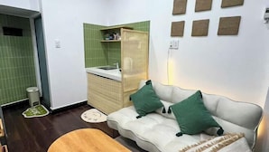 A compact living space with a kitchenette, a sofa with green cushions, and a woven basket. - Small Private house in Bui Vien Walking Street (Ho Chi Minh City)