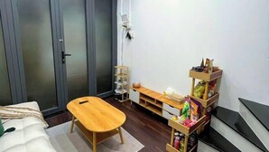 A compact room with a bed, a small wooden table, a TV, and a shelf with snacks. - Small Private house in Bui Vien Walking Street (Ho Chi Minh City)