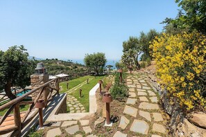 A stone pathway leading to a pool area with a wooden deck and a view of the sea.