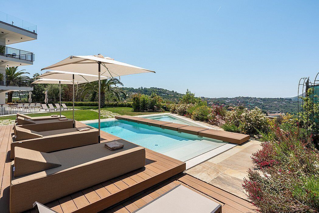 A swimming pool with sun loungers and umbrellas, surrounded by a landscaped garden and a view of the hills.