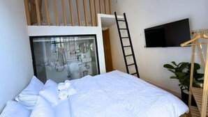 Ein Schlafzimmer mit einem Bett, einem an der Wand montierten Fernseher, einer Leiter und einer Pflanze.