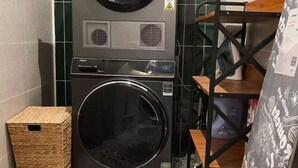 Ein Waschraum mit einer Waschmaschine mit Frontlader, einem Korbwäscheschrank und einem Metallregal mit einem gemusterten Stoff.