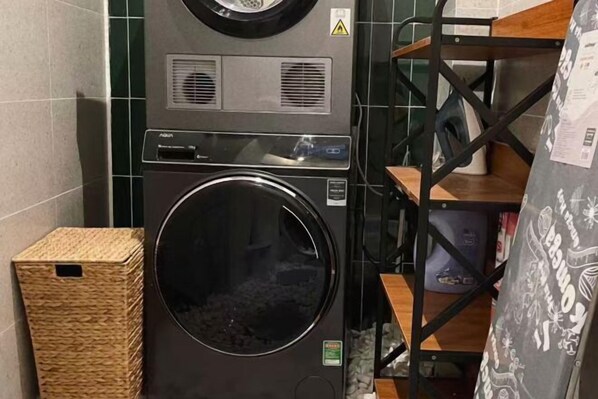 A laundry room with a front-loading washing machine, a wicker basket, and a metal shelving unit with a patterned cloth. - LYLAC Home Saigon HHH - Beautiful City Center Whole Townhouse in D1 (Ho Chi Minh City)