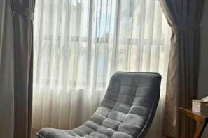 A room with a large window covered by sheer curtains, a dark leather armchair, and a small wooden side table with a lamp. - LYLAC Home Saigon HHH - Beautiful City Center Whole Townhouse in D1 (Ho Chi Minh City)