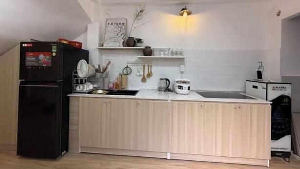 A modern kitchen with a black refrigerator, wooden cabinets, a white countertop, and a built-in sink. - LYLAC Home Saigon HHH - Beautiful City Center Whole Townhouse in D1 (Ho Chi Minh City)