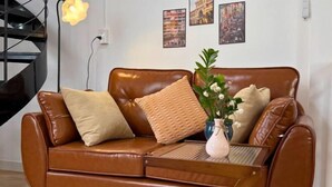 A brown leather sofa with cushions, a small wooden side table, and a vase with flowers. - LYLAC Home Saigon HHH - Beautiful City Center Whole Townhouse in D1 (Ho Chi Minh City)