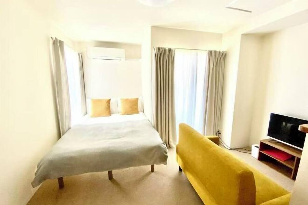 Ein Hotelzimmer mit einem Bett, einem gelben Sofa, einem Fernseher und Vorhängen.