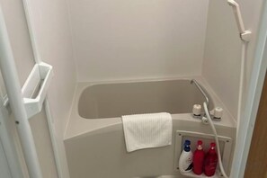 A small, enclosed shower area with a bathtub, a towel, and toiletries. - LuckyHouse yorokobiya 901 (Osaka)