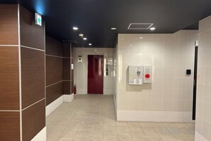 Ein Hotelgang mit einem Feuerlöscher, einer roten Tür und einem an der Wand befestigten Infobildschirm.
