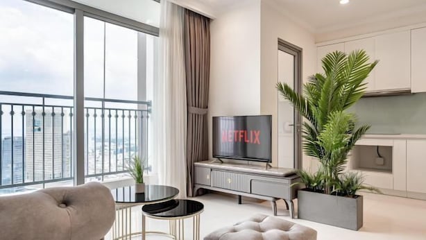 Ein modernes Wohnzimmer mit Sofa, Fernseher, kleinem Tisch und einem Balkon mit Blick auf die Stadt.