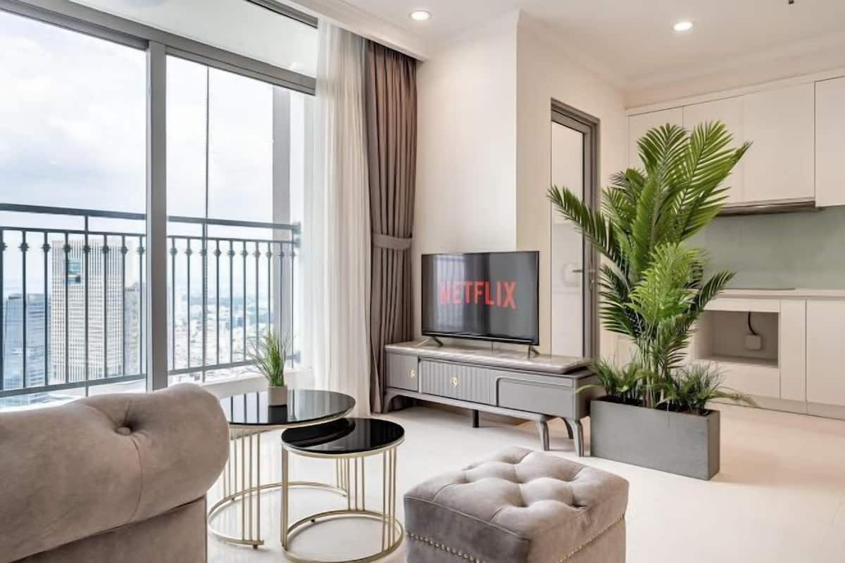 A modern living room with a sofa, a TV, a small table, and a balcony with a view of the city.