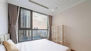 Ein Hotelzimmer mit großem Fenster, einem Bett, einer weißen Regaleinheit und Blick auf die Stadt.