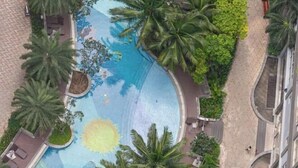 Luftaufnahme eines Resorts mit einem zentralen Swimmingpool, umgeben von Palmen und Liegebereichen.