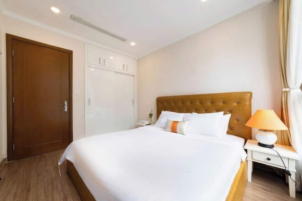 A hotel room with a large bed, a wooden door, a wardrobe, and a bedside lamp.
