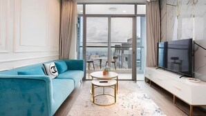 Ein modernes Wohnzimmer mit einem blauen Sofa, einem runden Couchtisch, einem Fernseher und einem großen Fenster mit Blick auf die Stadt.