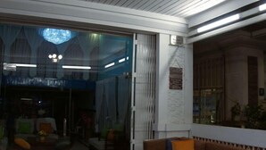 A living room with a brown sofa, a glass door leading to another room, and a white wall with a framed picture. - Haven Inn (Phnom Penh)