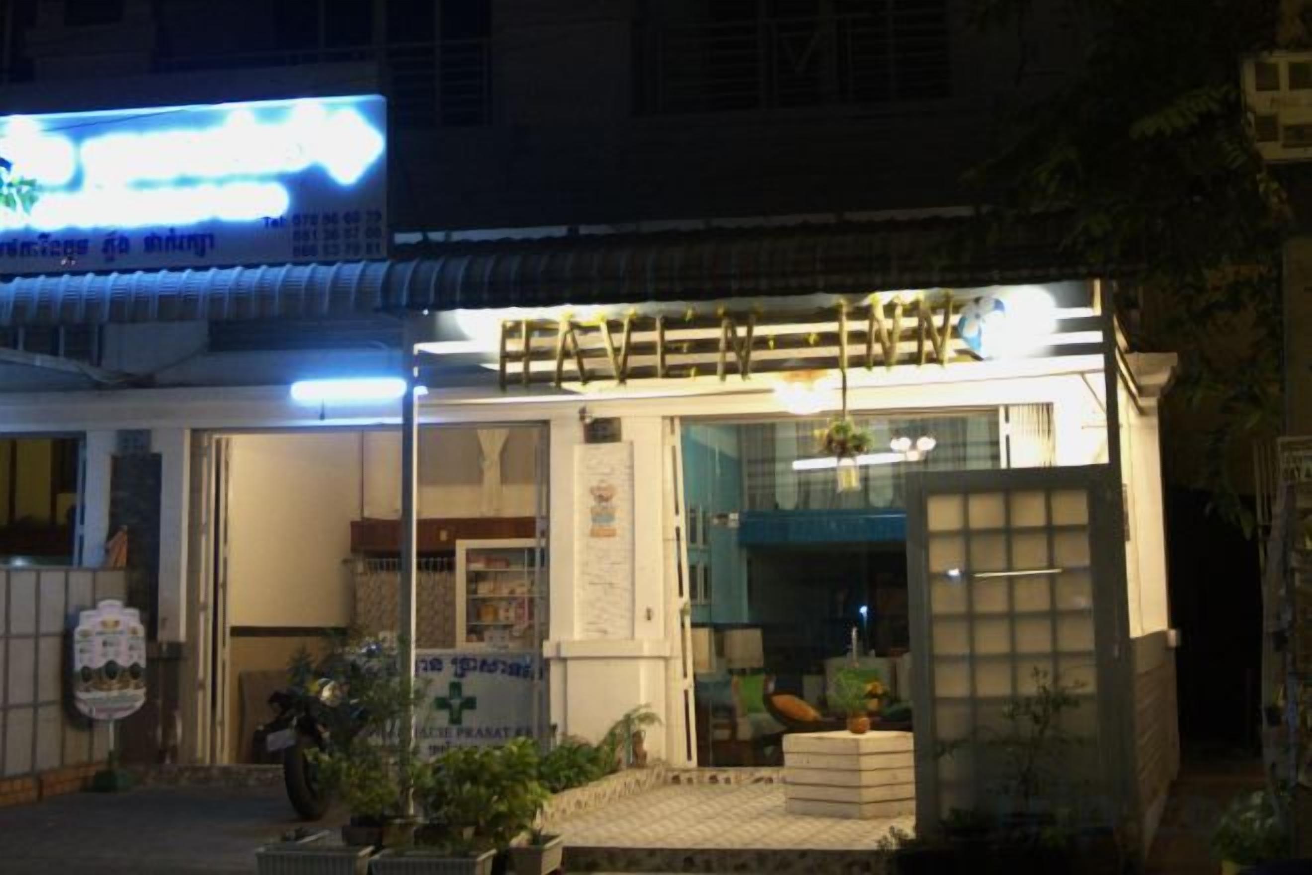 A building with a signboard, a motorcycle parked in front, and a small garden area.