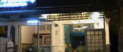A building with a signboard, a motorcycle parked in front, and a small garden area.
