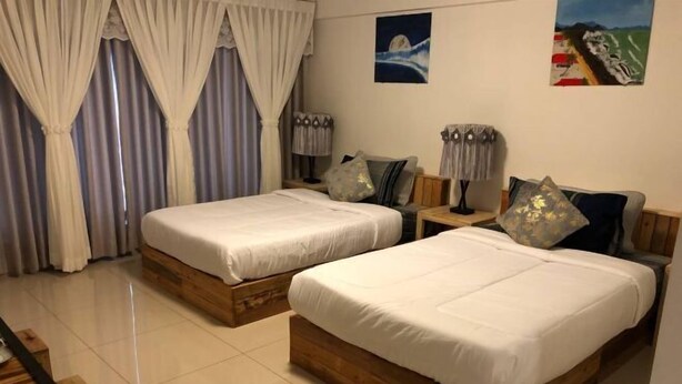 A hotel room with two wooden beds, a nightstand, a lamp, and a painting on the wall. - Haven Inn (Phnom Penh)