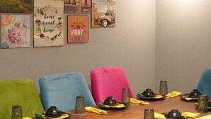 A dining area with a wooden table set for four, colorful chairs, and wall art with motivational phrases. - Haven Inn (Phnom Penh)