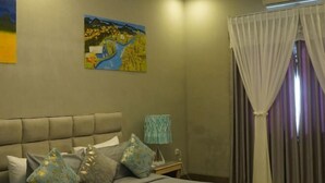 A bedroom with a bed, pillows, a nightstand, an air conditioner, and a painting on the wall. - Haven Inn (Phnom Penh)