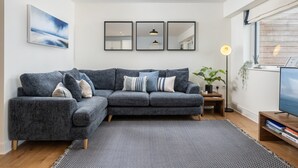 Un salon moderne avec un canapé d’angle gris, un tapis noir et blanc, une grande fenêtre offrant une belle vue et un téléviseur à écran plat.