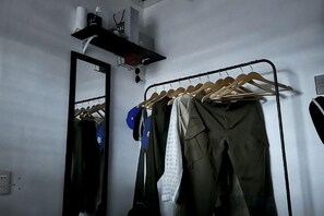 Une pièce comprenant un portant en métal pour suspendre les vêtements, un miroir et une étagère sur laquelle se trouve un rouleau d’essuie-tout.