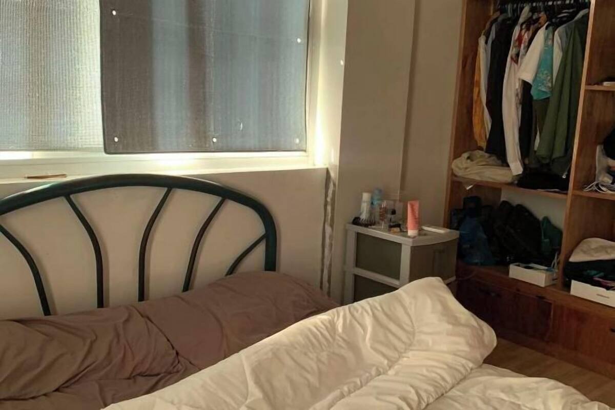 A bedroom with a bed, a window, a closet, and a small bedside table.