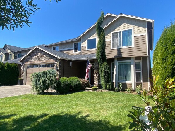 A two-story residential house with a garage, a well-maintained lawn, and an American flag.