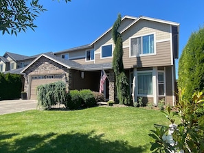 A two-story residential house with a garage, a well-maintained lawn, and an American flag. - Beautiful 4BR Home in E Vancouver 30+ Day Stays Near PDX, Costco & Hospitals (Vancouver)