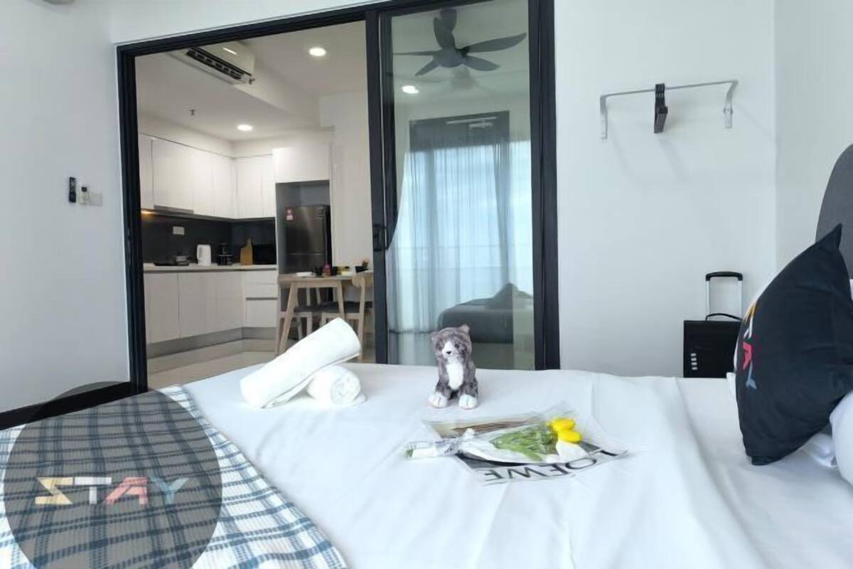 A hotel room with a bed, a small desk, a kitchenette in the background, and a sliding glass door.