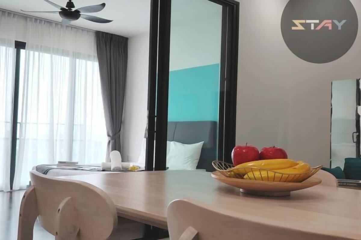 A modern hotel room with a dining table, a bowl of fruit, and a large mirror.