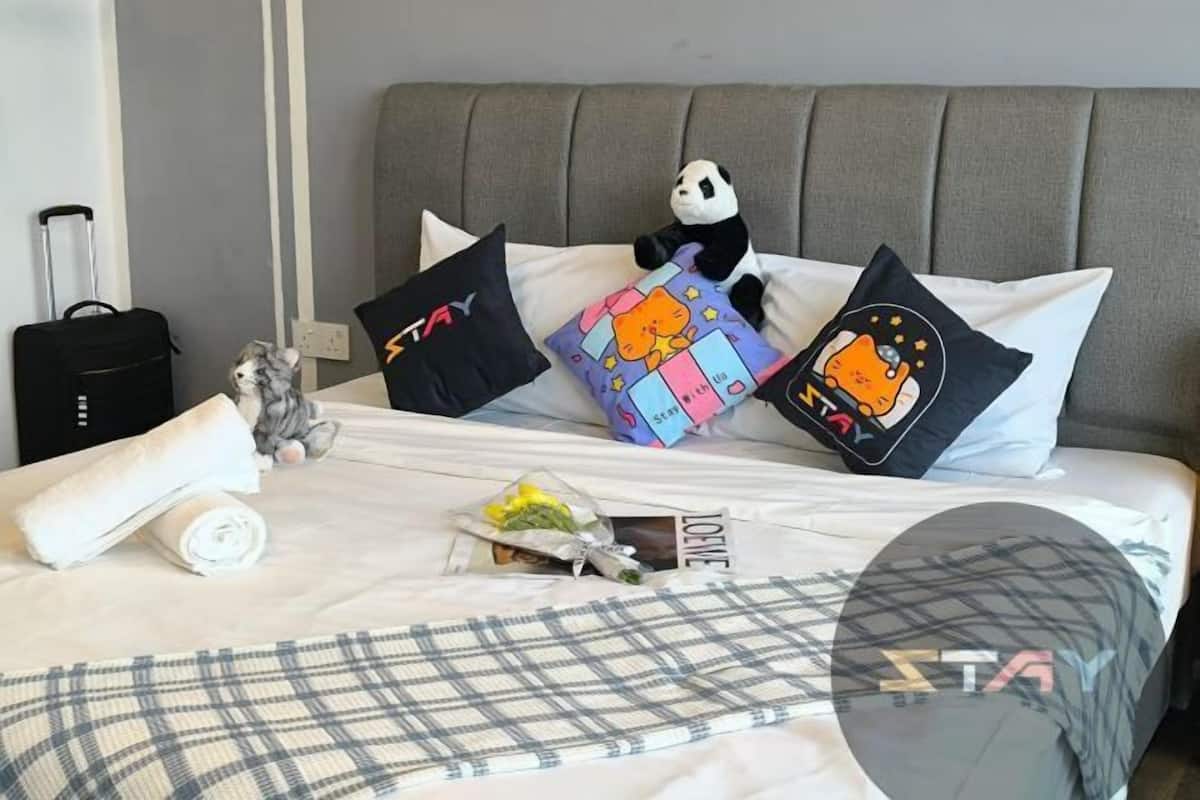 A neatly made bed with a plaid blanket, pillows with various designs, a stuffed panda toy, a rolled towel, and a small statue.