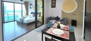 Habitación de hotel con cama, sofá, mesa de comedor con platos y tazas, y vista a la ciudad.