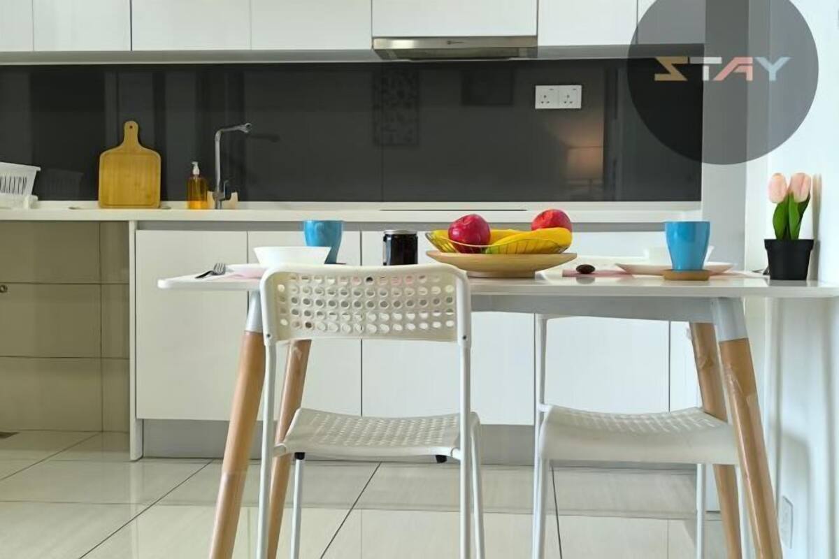 A modern kitchen with white cabinets, a black backsplash, a wooden cutting board, a fruit bowl, and a blue cup.