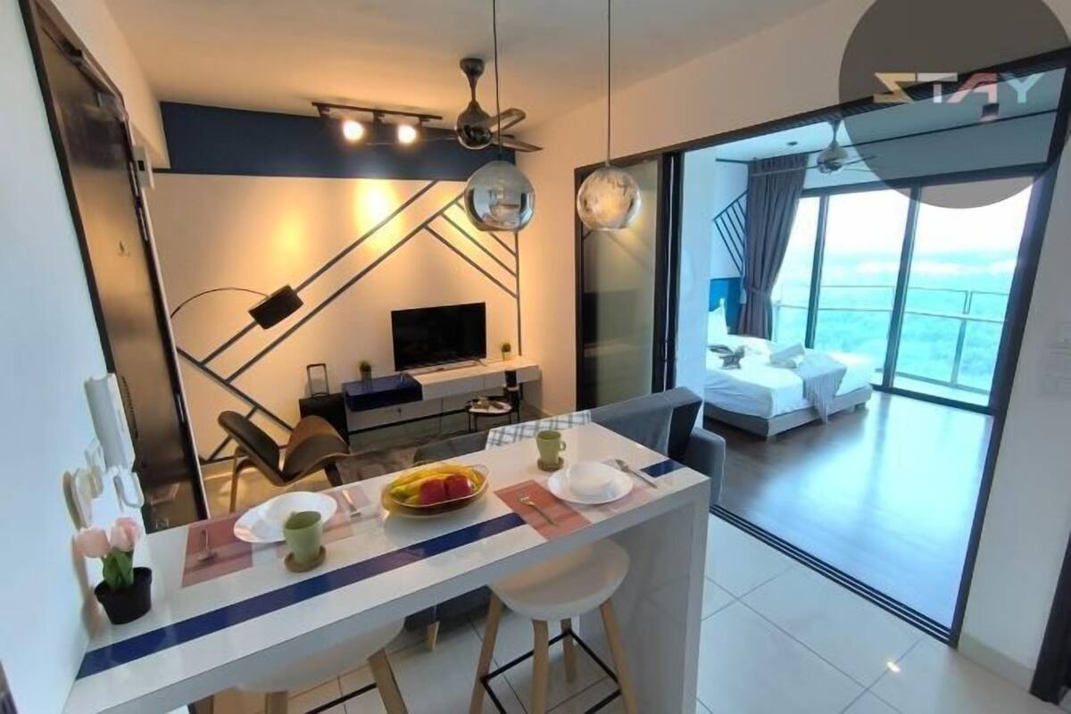 A modern hotel room with a balcony, a dining area with a table and chairs, a TV, and a bed with a view.