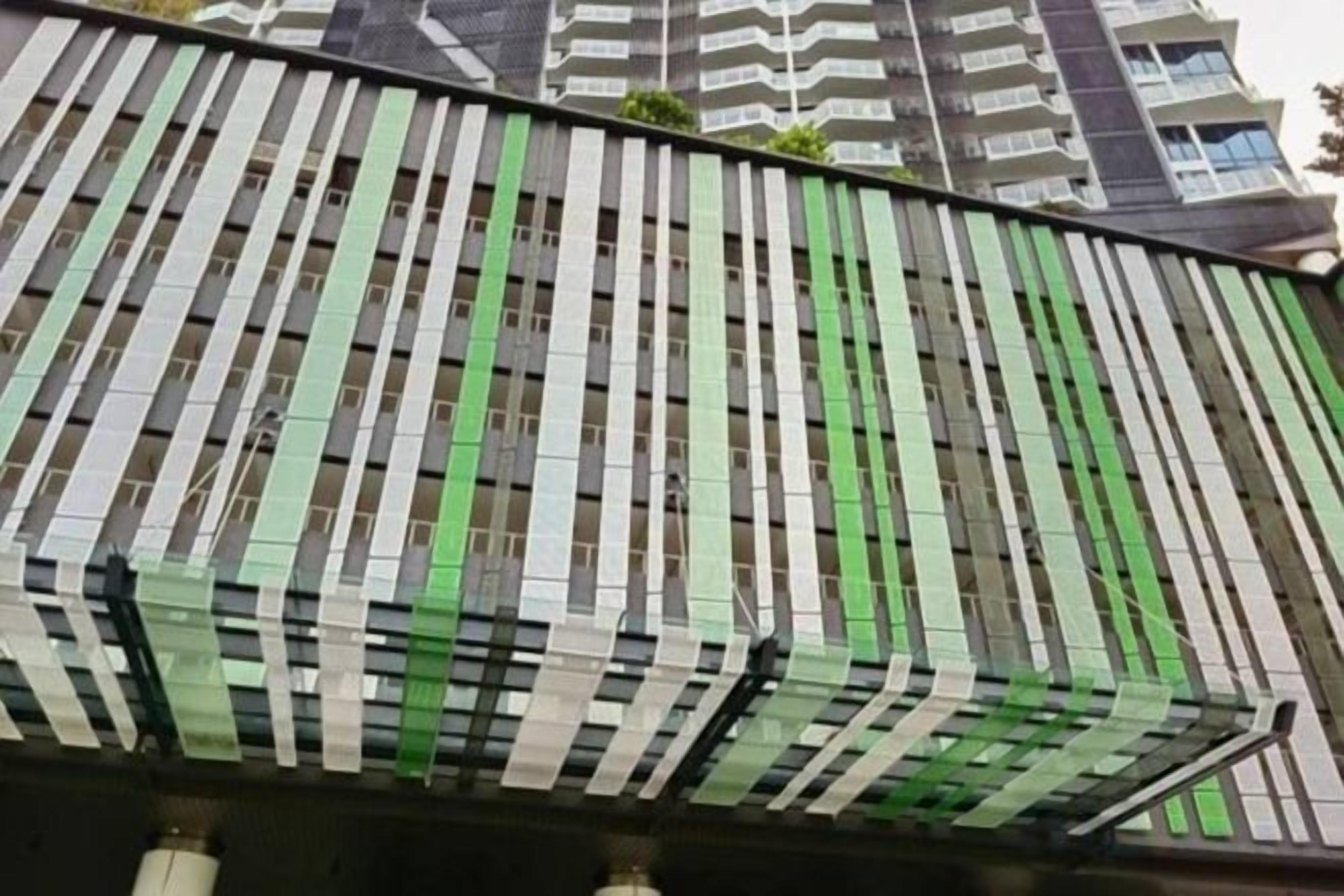 Une façade d’immeuble avec des rayures verticales vertes et blanches, une ligne de toit incurvée et une série de fenêtres.