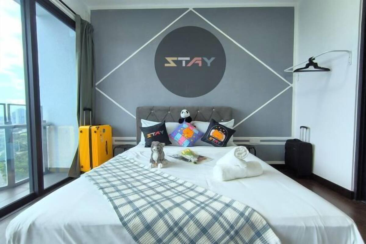 A hotel room with a bed, a 'STAY' sign on the wall, a window, and a view of the city.