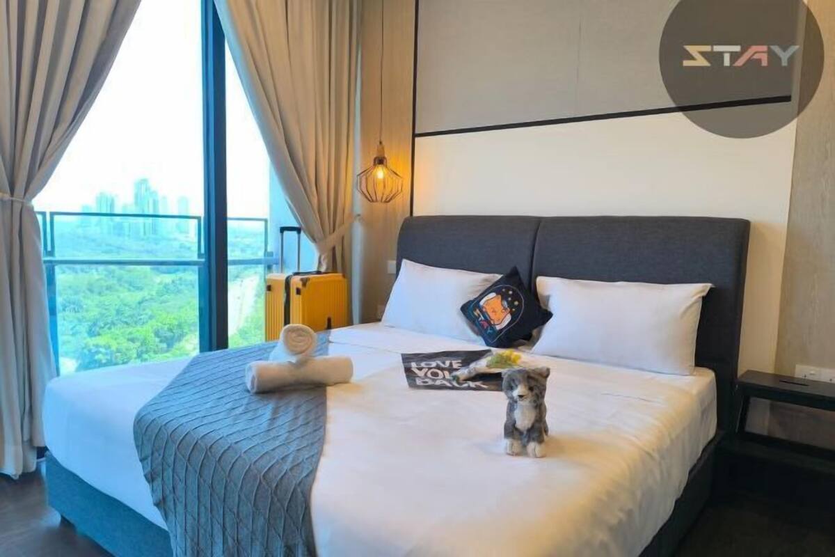 A hotel room with a large bed, a view of the city, and a 'STAY' sign on the wall.