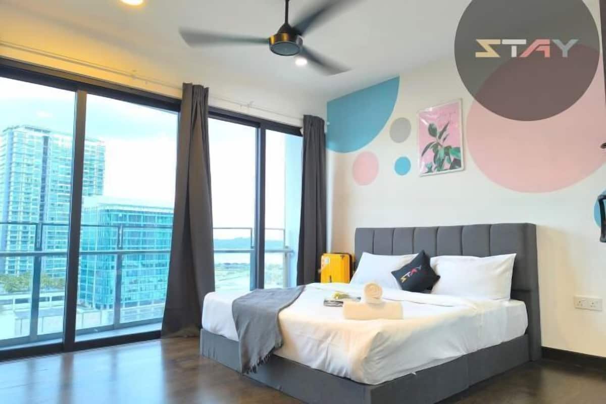 A modern hotel room with a large bed, a ceiling fan, and a view of a cityscape through large windows.