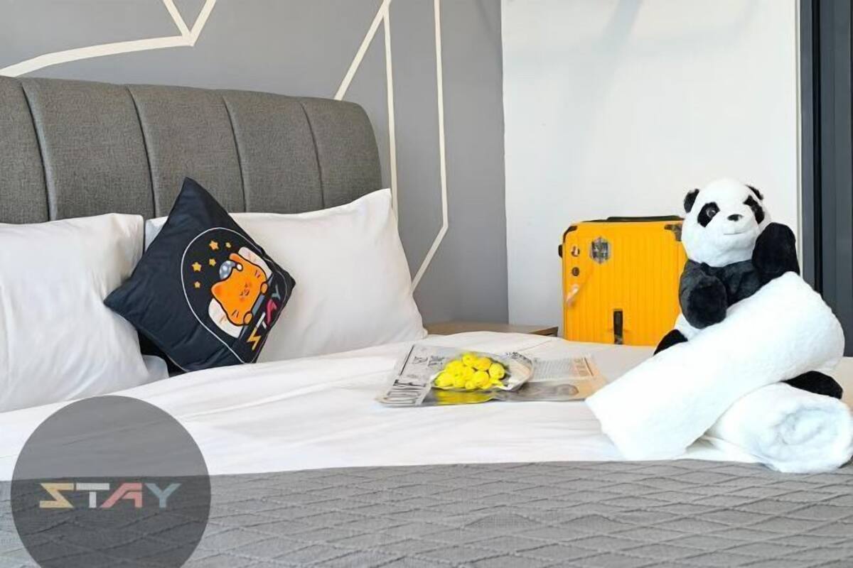 A hotel room with a bed, pillows, a stuffed panda toy, a suitcase, and a newspaper.