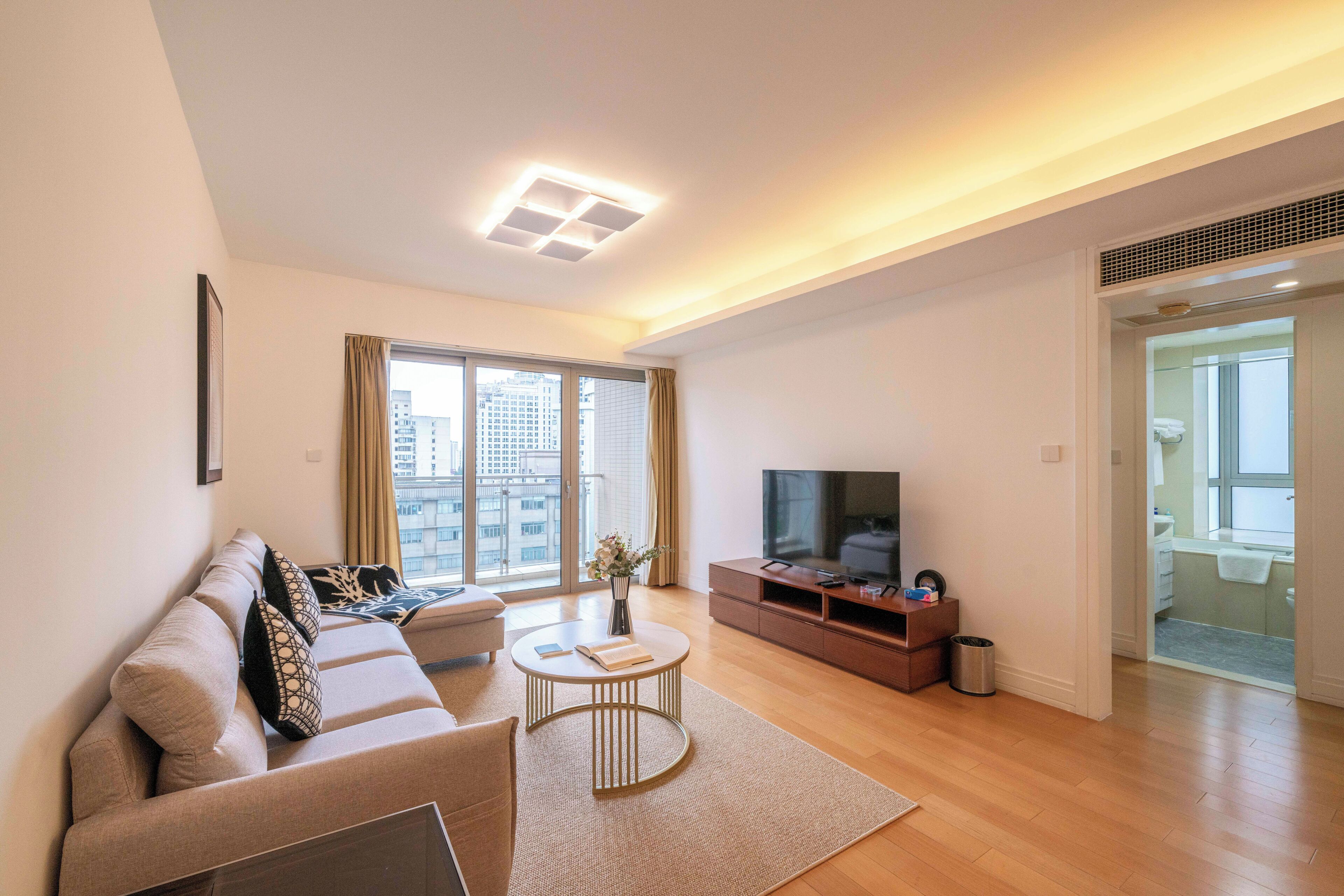 Una sala de estar moderna con un sofá, una mesa de centro, televisor y vistas a la ciudad a través de amplios ventanales.