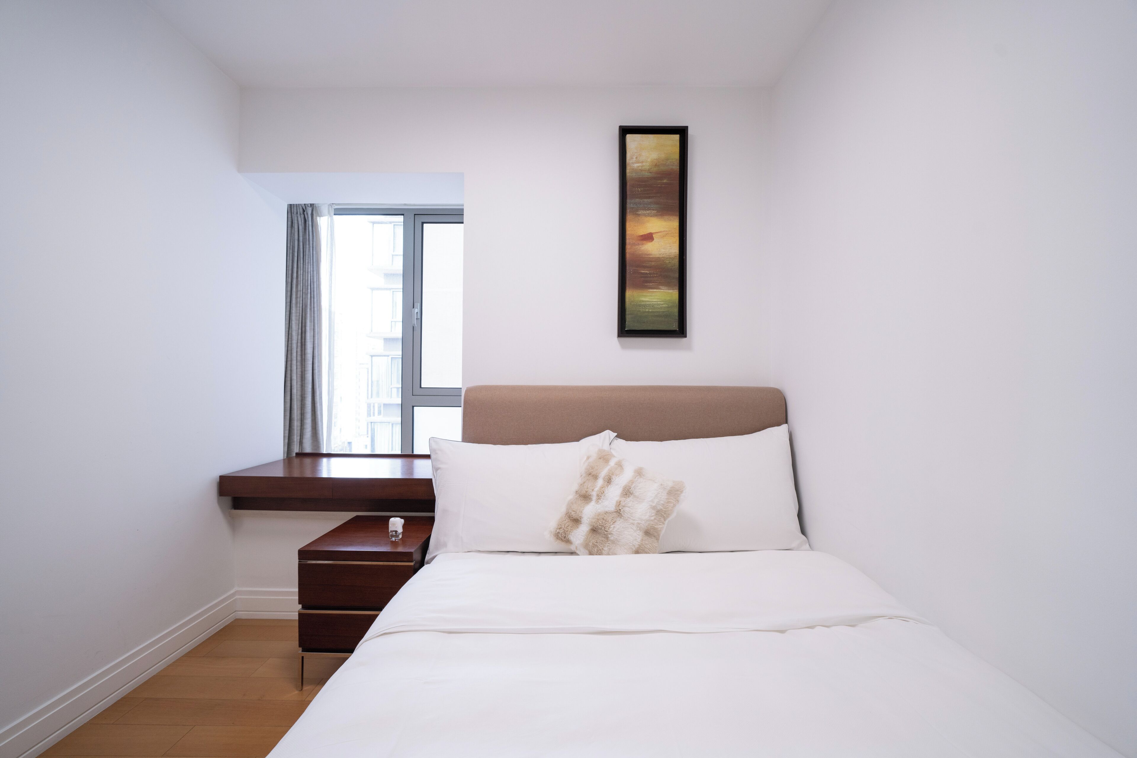 Un dormitorio con cama, mesita de noche, ventana y un cuadro en la pared.
