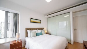 Un dormitorio con cama, mesita de noche, cómoda, ventana con cortinas, un cuadro en la pared y armario de puertas correderas.