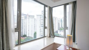 Habitación con ventanas amplias que ofrecen vistas a la ciudad, una mesita de noche con lámpara y un diseño limpio y minimalista.