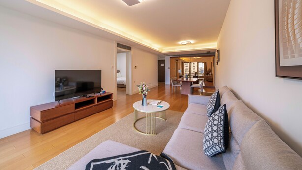 Una sala de estar moderna con un televisor de pantalla plana, un mueble de entretenimiento de madera y un sofá color beige con cojines estampados.