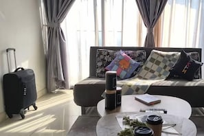Et værelse med sofa, sofabord, kuffert og et vindue med gardiner.